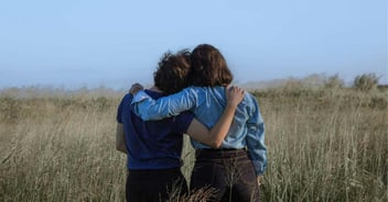 Two people face away from the camera and hug sideways